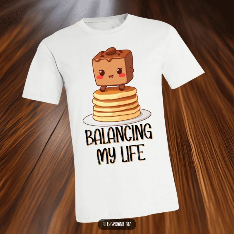 Funny t-shirt showing a brownie character grinning while balancing on a wobbly stack of pancakes, embodying playful precariousness.